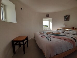 A bedroom with a bed, a small table, a window, and a nightstand.