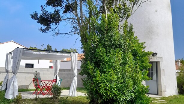 Un bâtiment blanc avec une tour circulaire, un petit arbre et une chaise rouge placée sous un auvent blanc.
