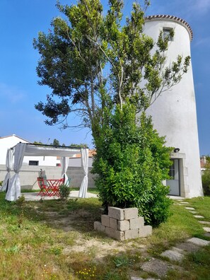 Un bâtiment blanc avec une tour circulaire, un petit arbre et une chaise rouge placée sous un auvent blanc.