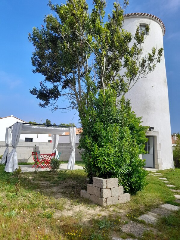 A white building with a circular tower, a small tree, and a red chair under a white canopy.