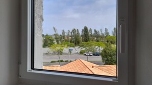 Une fenêtre donnant sur un parking, des arbres et un bâtiment avec un toit recouvert de tuiles.