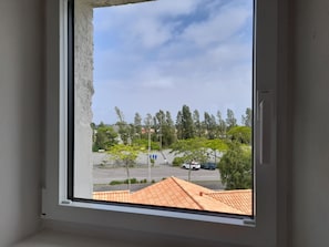 Une fenêtre donnant sur un parking, des arbres et un bâtiment avec un toit recouvert de tuiles.