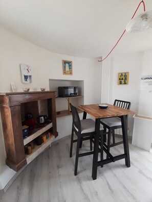 A compact kitchen with a wooden table and chairs, a microwave, a kettle, and a shelf with mugs.