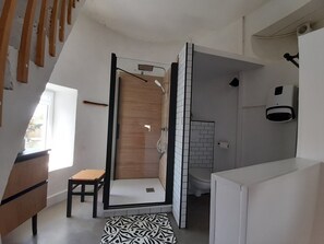 A modern bathroom with a shower, toilet, and a small seating area.