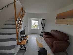 Ett vardagsrum med en trappa, en brun lädersoffa, ett träbord och en svart golvlampa.