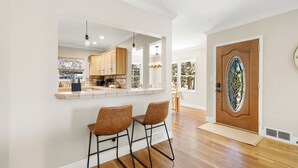 A kitchen with wooden cabinets, a bar area with two chairs, and a large wooden door with a stained glass window.