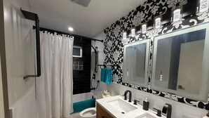 Een badkamer met een bad, twee wastafels, een toilet en een douche.