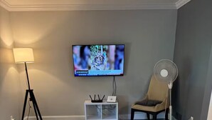 Ett vardagsrum med en soffa, en tv, en lampa, en fläkt och en fjärrkontroll.
