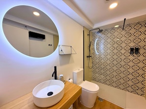 Um banheiro moderno com espelho redondo, pia branca, vaso sanitário e chuveiro com azulejos estampados.