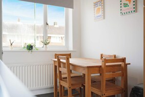 A wooden dining table with four chairs, a window with a view of buildings, and a radiator below the window. - Spacious 4BR Home Sleeps 8 by Stay With Us (County Durham)
