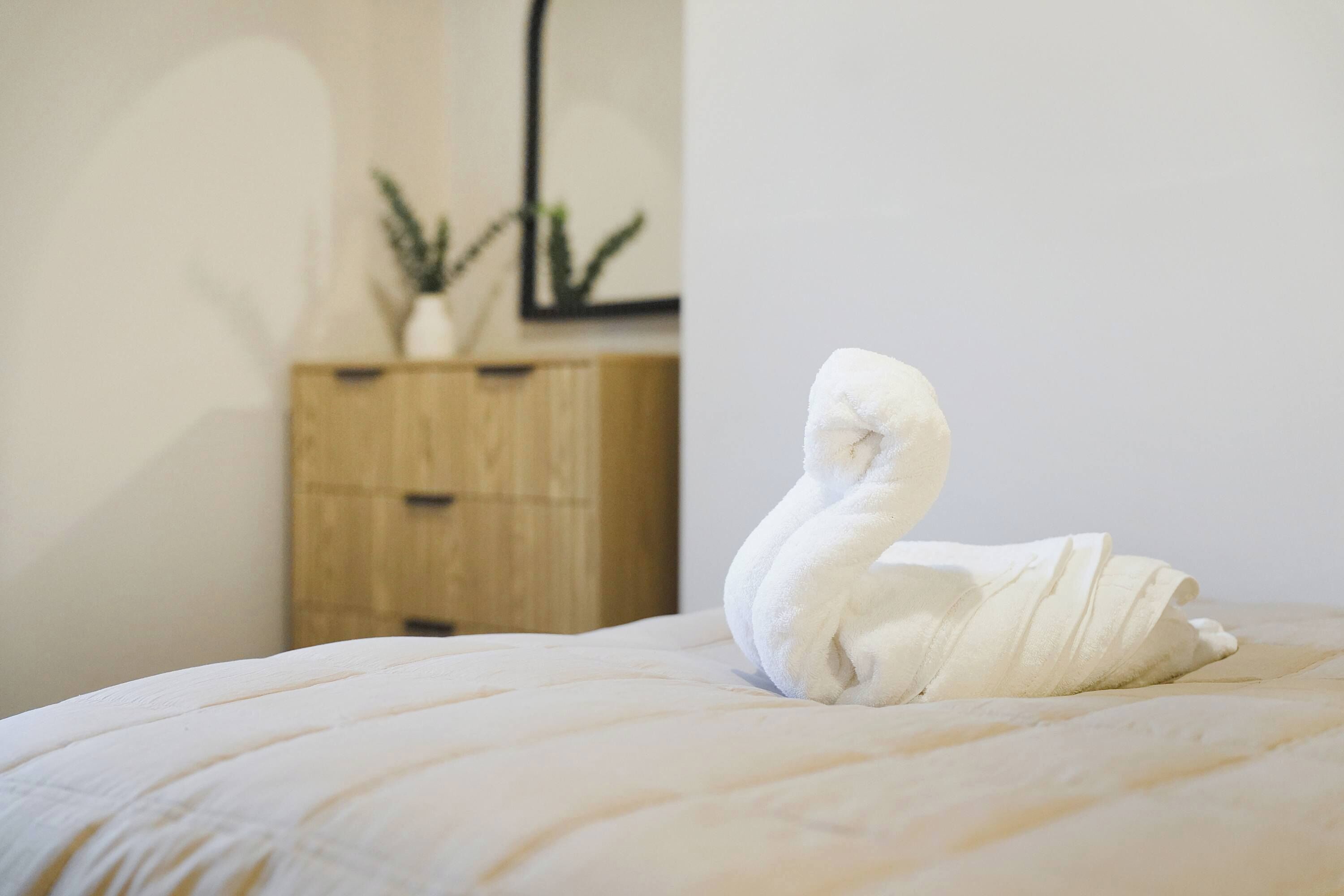 Toalha em formato de cisne sobre a cama num quarto com um armário de madeira e um quadro na parede.