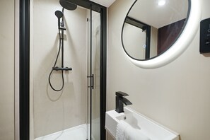 A modern bathroom with a glass-enclosed shower, a white sink, and a round mirror. - Bright 4BR Norton Getaway Sleeps 7 by Stay With Us (Stockton-on-Tees)