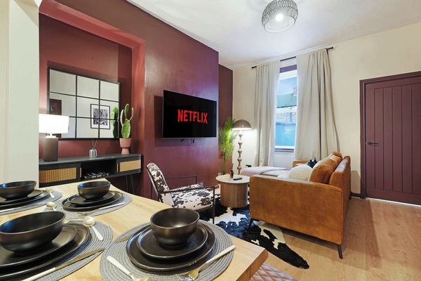 Designed for shared moments, this dining area features a practical table with bench seating alongside a comfortable living space. The nearby sofa and wall-mounted TV create an inviting setting for relaxing after meals.