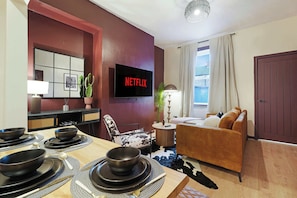 Un salon moderne avec un téléviseur à écran plat, un canapé, une table à manger dressée avec des bols et des assiettes, et un mur d’accent rouge.