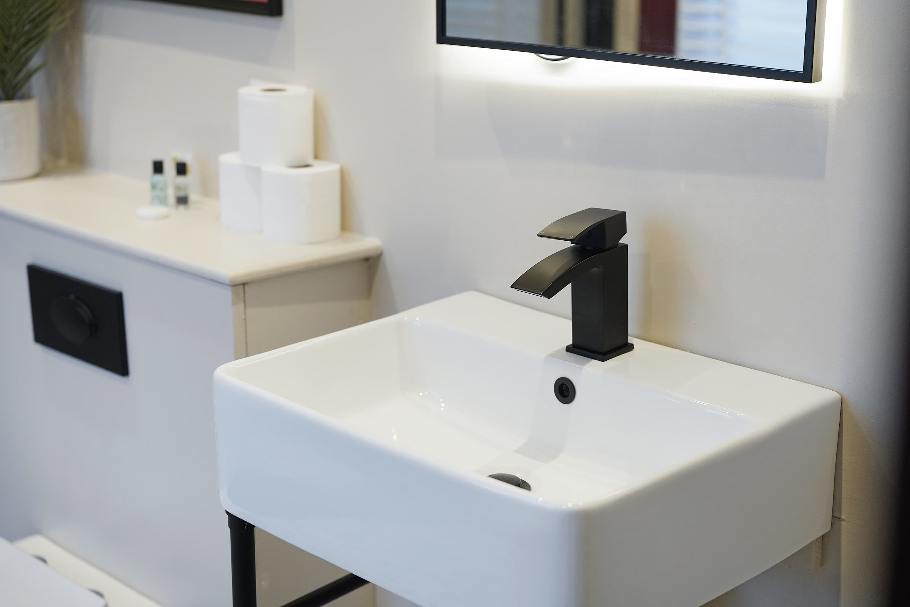 Een moderne badkamer met een wit wastafelmeubel, een zwarte kraan en een spiegel erboven.