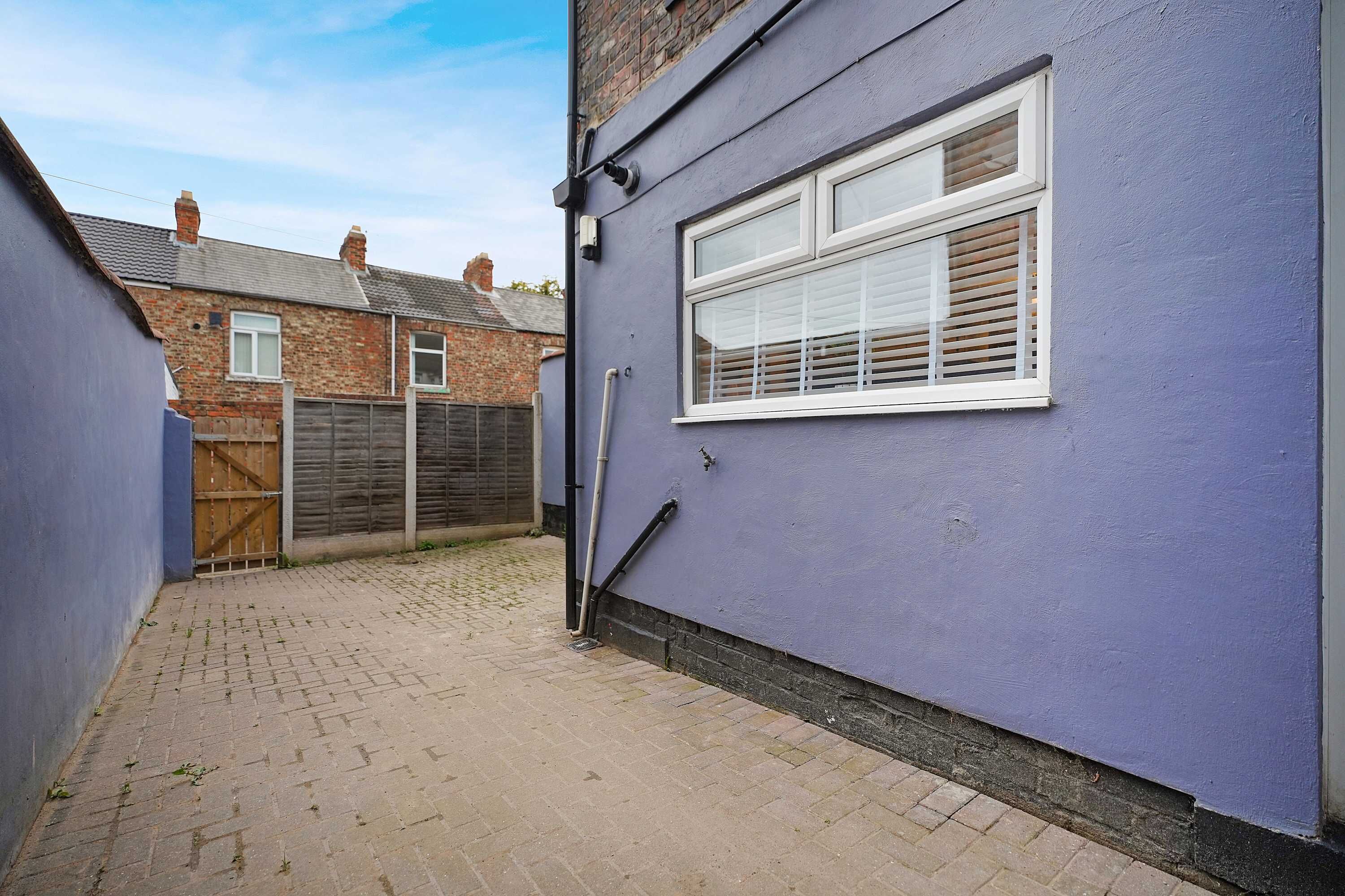 A narrow alleyway with a blue wall and a window with white shutters.