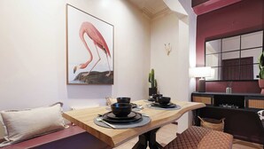 Un'area pranzo con un tavolo di legno apparecchiato per due persone, una panca imbottita, una pianta di cactus e un'opera d'arte a parete raffigurante un flamingo.