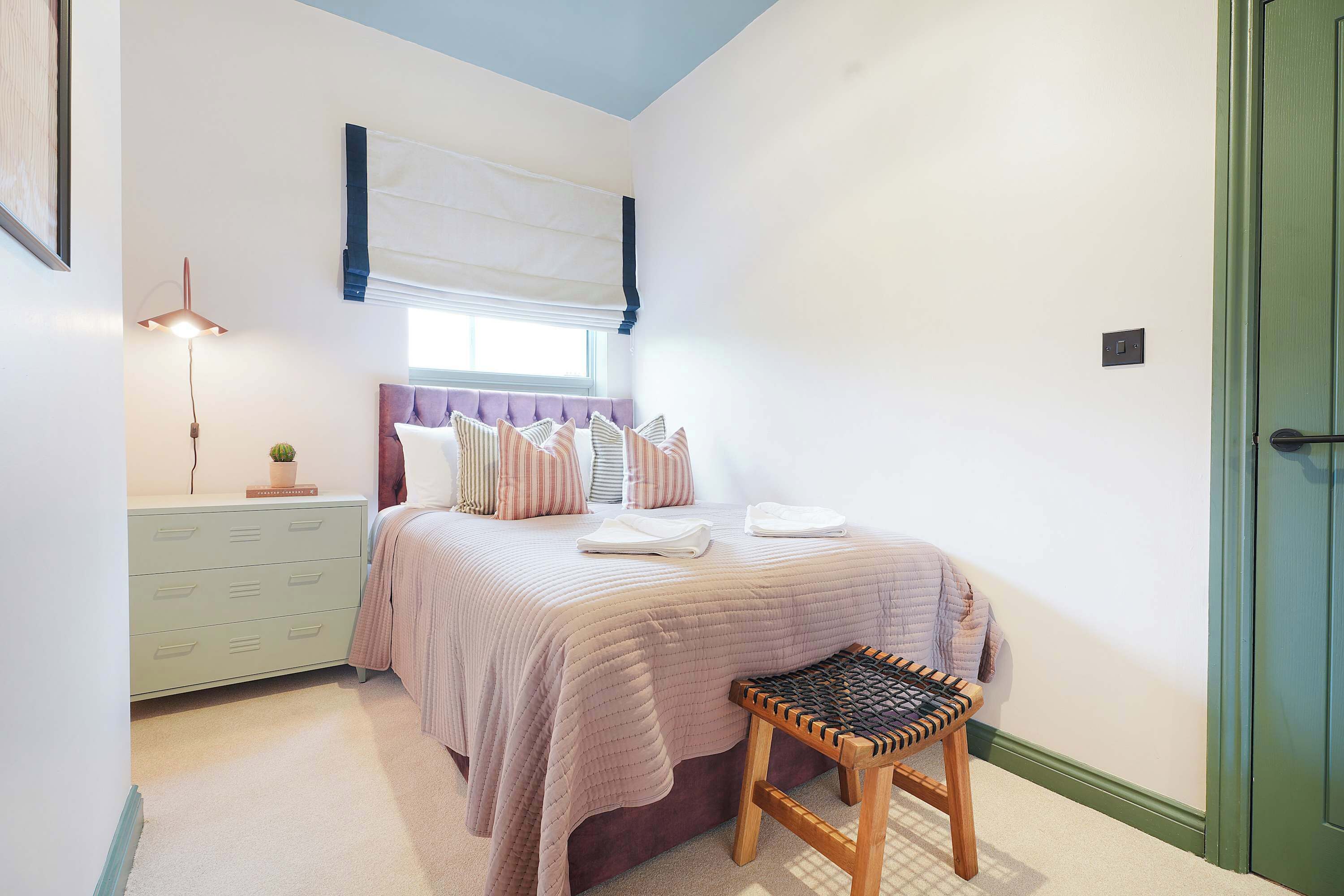 Un dormitorio con cama, mesita de noche, lámpara y ventana con persianas.