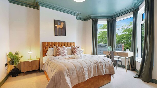 Un dormitorio con una cama grande, mesitas de noche, un escritorio y una ventana con cortinas.