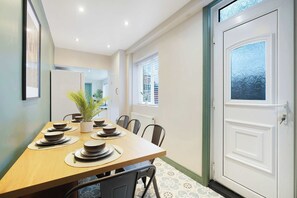 Un comedor con una mesa de madera dispuesta para una comida, sillas, una planta en maceta y una puerta blanca con un panel de vidrio esmerilado.