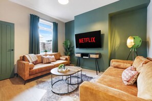 Una sala de estar con un sofá, una mesa de centro y un televisor mostrando 'NETFLIX'.