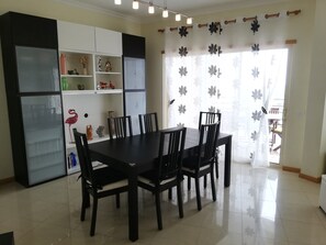 Ein Essbereich mit Tisch und Stühlen, ein weißes Schrank mit Regalen und ein Fenster mit Blumenmuster-Vorhang.