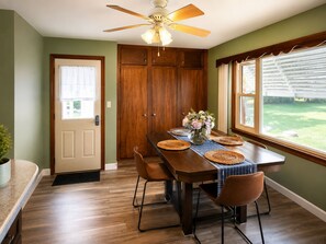 A dining area with a wooden table, chairs, a ceiling fan, and a view of a green lawn.