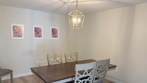 Un comedor con una mesa de madera, sillas blancas y una lámpara colgante.