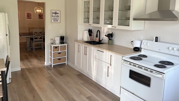 Una cocina moderna con armarios blancos, estufa empotrada y comedor con mesa y sillas de madera.