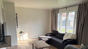 Una sala de estar moderna con un sofá, una mesa de centro, un televisor y un ventanal con cortinas.