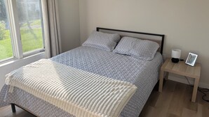 Un dormitorio con cama, mesita de noche, lámpara y ventana con cortinas.