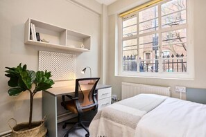 Ein Schlafzimmer mit Bett, Schreibtisch, Stuhl, Regalen und einem Fenster mit Aussicht.