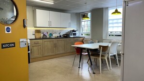 A compact kitchen with wooden cabinets, a microwave, and a dining area with a table and chairs. - Cosy Private Double in Westminster – Steps from Big Ben & Buckingham Palace (London)