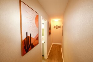 Ein Korridor mit Holzboden, einer Tür zu einem Badezimmer und zwei an der Wand befestigten Kunstwerken.