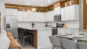 Una cucina moderna con mobili bianchi, un'isola centrale e un'area pranzo con sedie.