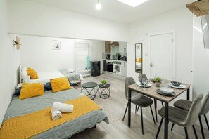 Ein modernes Hotelzimmer mit Bett, Nachttisch und einer kleinen Küchenzeile.