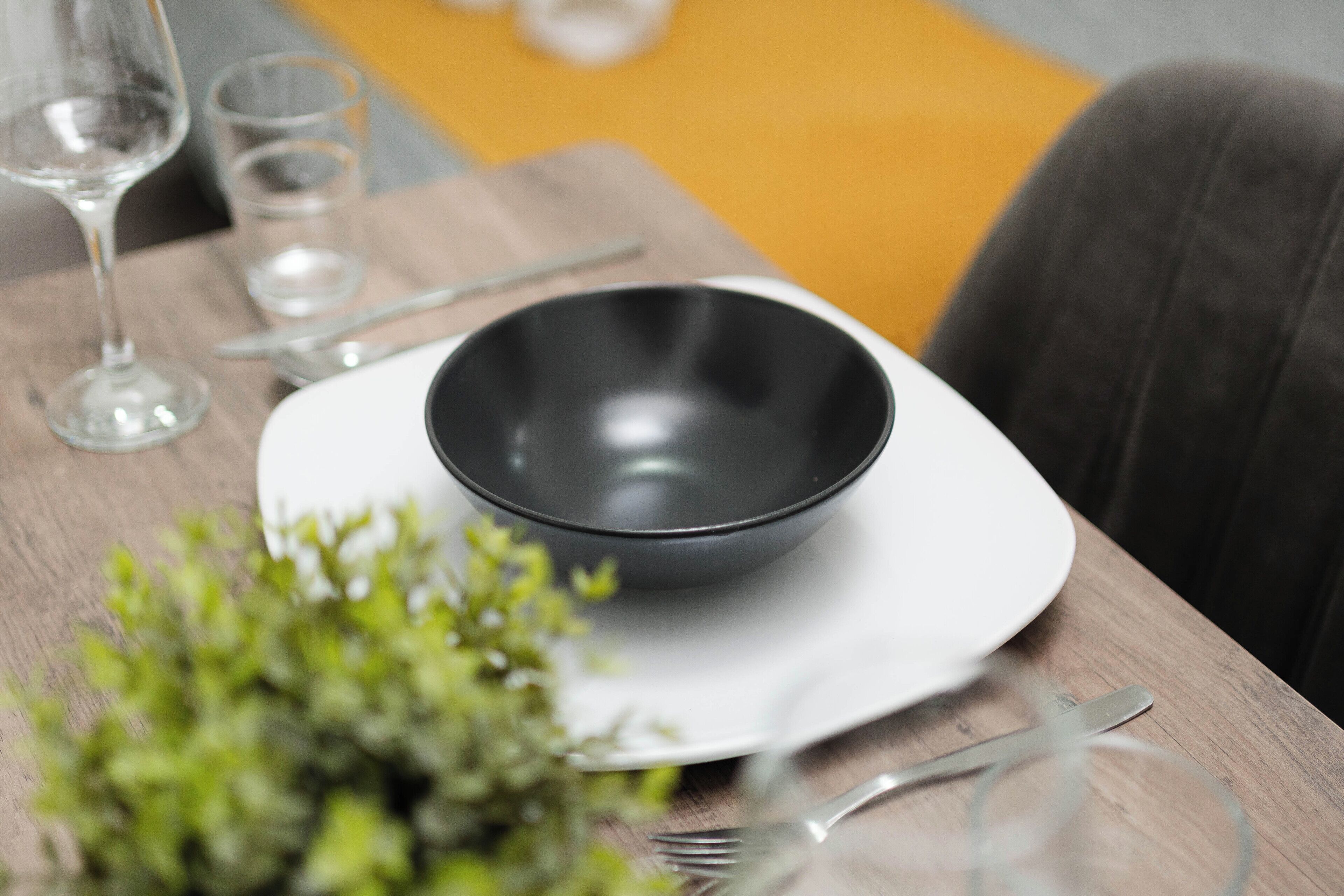 A dining table with a black bowl, a white plate, a fork, and a glass.