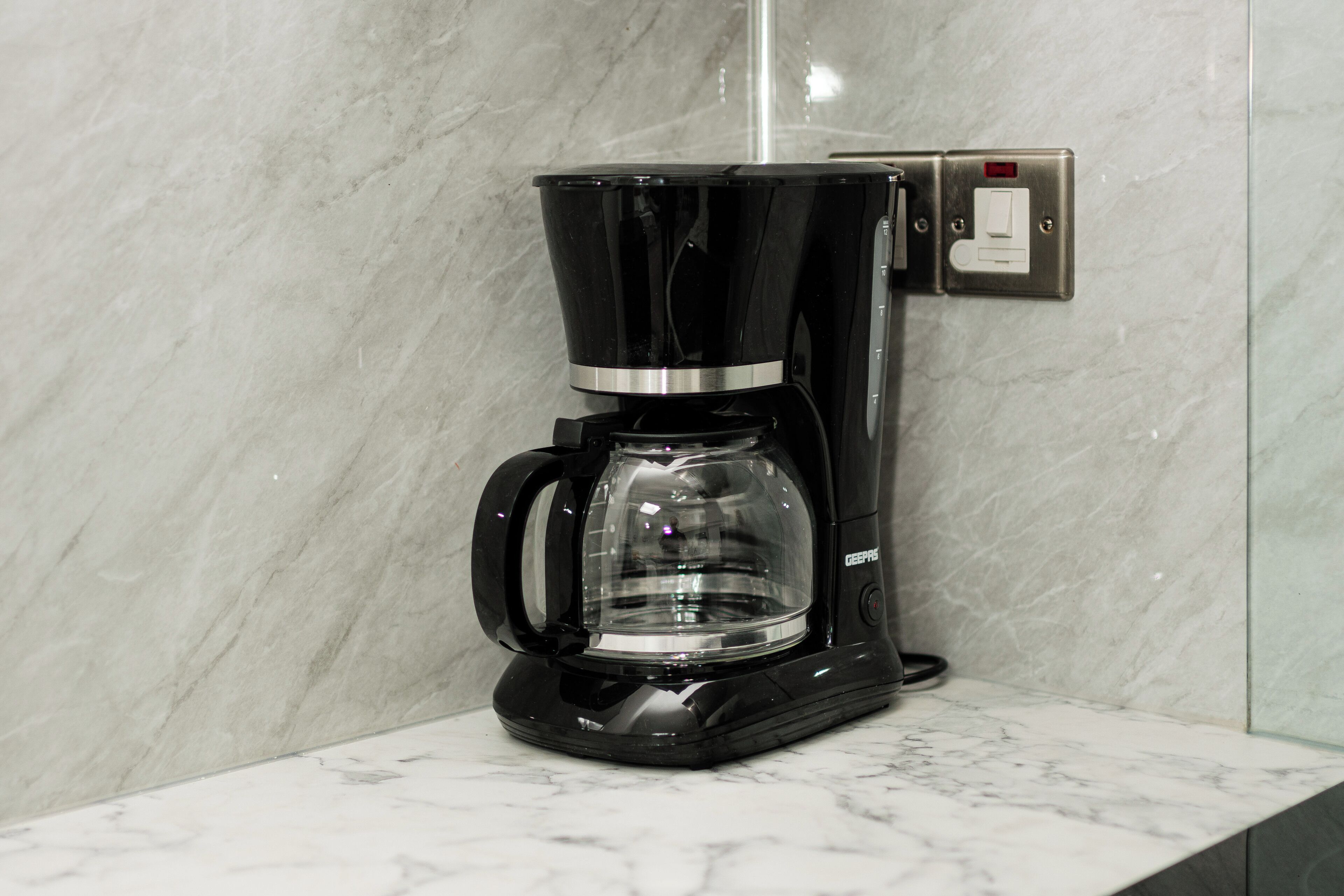 A black coffee maker with a clear carafe on a marble countertop.