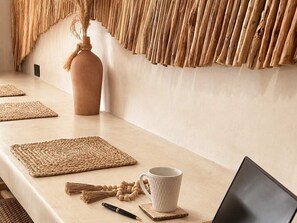 Une longue table de couleur claire, recouverte de sets de table en fibres tressées, avec une tasse blanche, un stylo et un ordinateur portable.