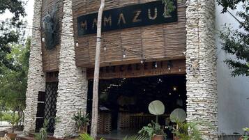 A building with a stone facade, a sign reading 'MAMA ZU', and outdoor seating with potted plants.