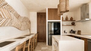 Eine moderne Küche mit Kochinsel, Holzkästen und einem Edelstahlkühlschrank, darüber eine Pendelleuchte.