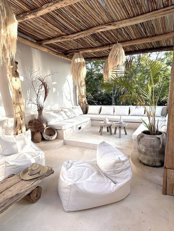 A covered outdoor seating area with white cushions, a woven ceiling, and potted plants. - Tulumaya Boho Luxe Villa in Aldea Zama Concierge (Tulum)
