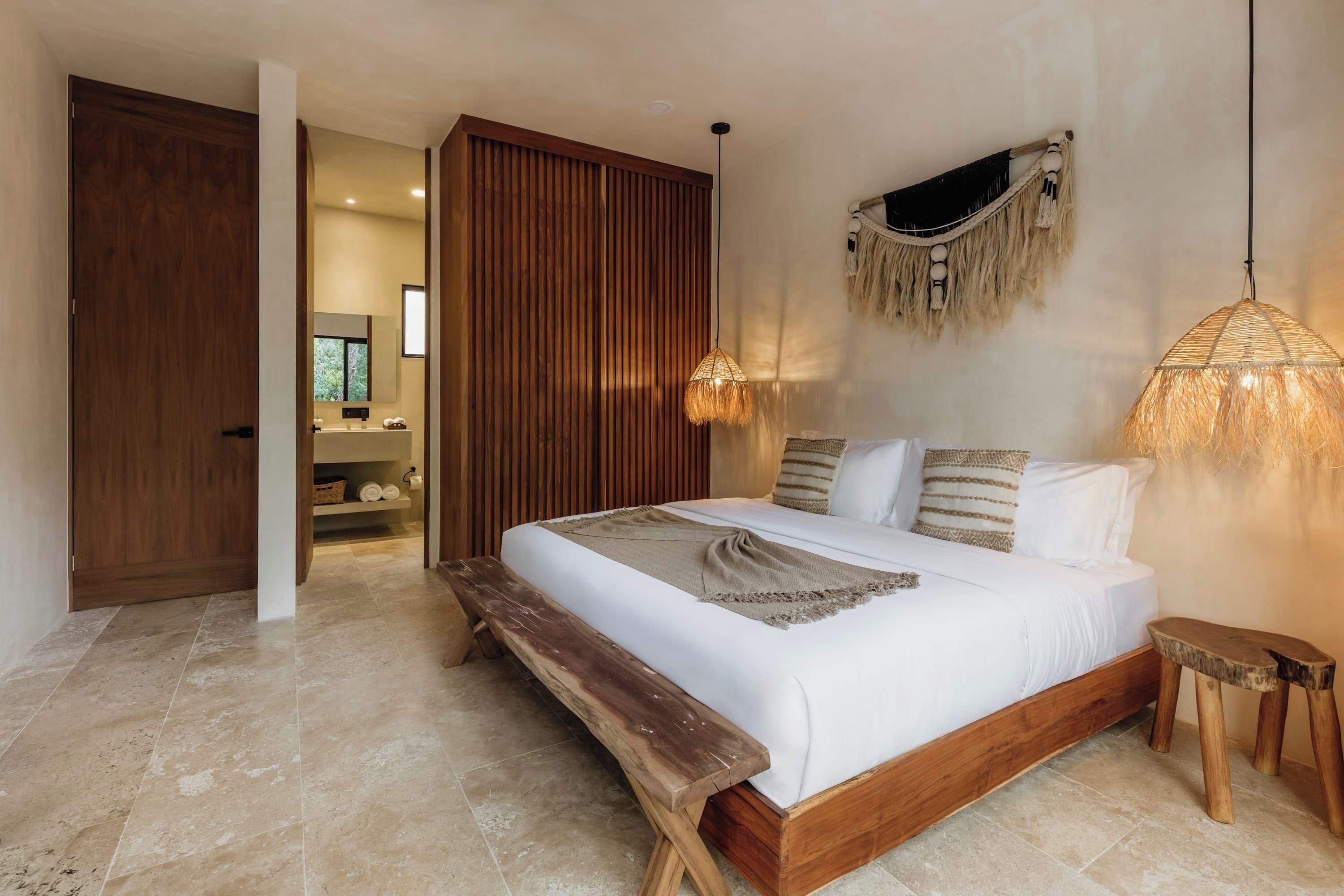 A bedroom with a wooden bed, a bench, a hanging light, and a wardrobe.