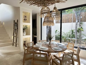 A dining area with a round wooden table, wicker chairs, and a hanging light fixture. - Tulumaya Boho Luxe Villa in Aldea Zama Concierge (Tulum)