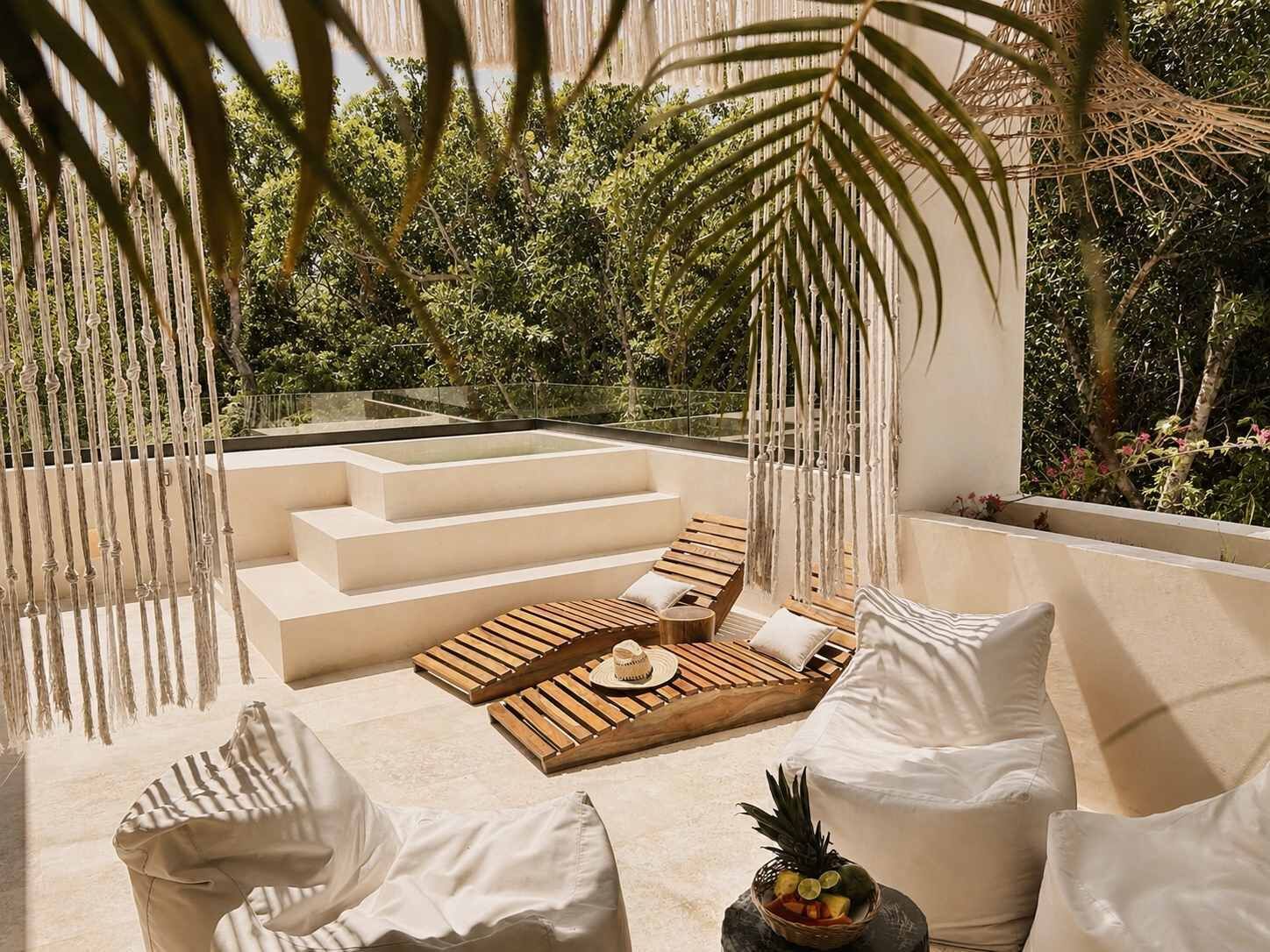 A sunlit outdoor seating area with a wooden deck, white cushions, and a fruit bowl.