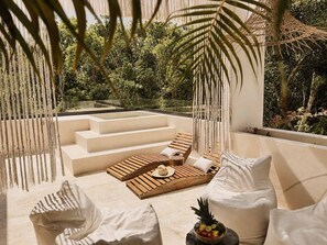 A sunlit outdoor seating area with a wooden deck, white cushions, and a fruit bowl. - Tulumaya Boho Luxe Villa in Aldea Zama Concierge (Tulum)