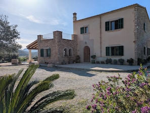 A stone building with a wooden door, green shutters, and a gravel courtyard. - Mallorcan house with pool, garden, barbecue and WIFI near the beach (Manacor)