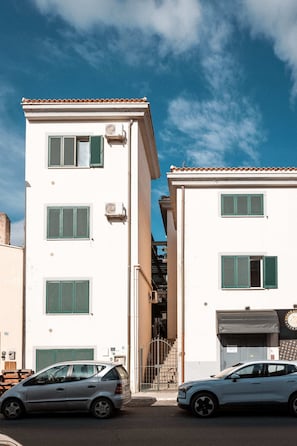 A white building with green shutters, a parked car, and a clear blue sky.