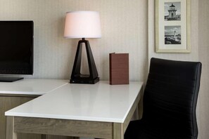 Ein Hotelzimmer mit Schreibtisch, Lampe, Stuhl, Fernseher und einem gerahmten Bild an der Wand.