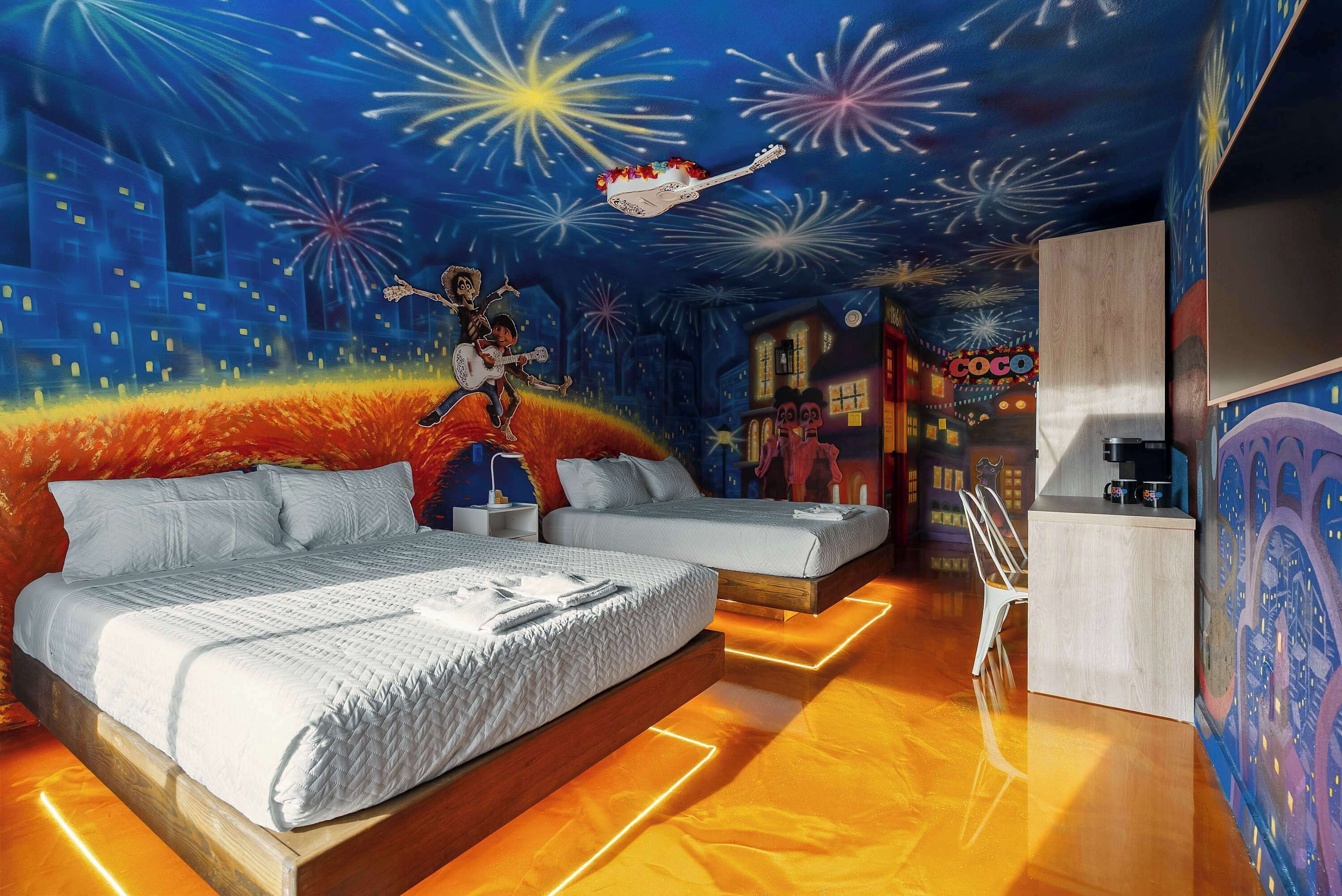 A bedroom with a bed, a nightstand, a dresser, and a mural of fireworks.